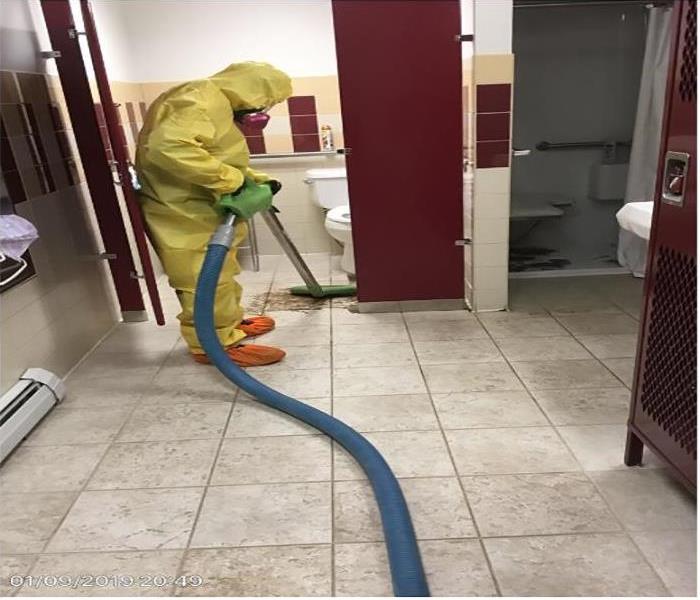 technician in yellow cleaning up sewage in men's locker room 