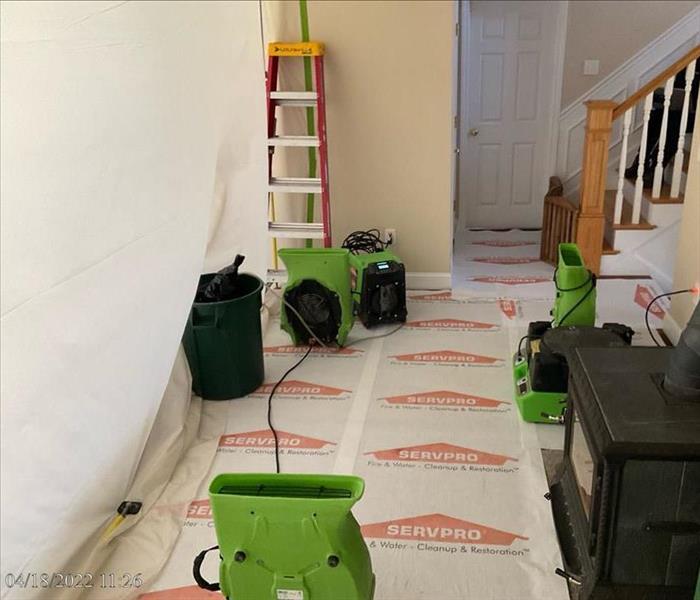 Covered floor with SERVPRO dehumidifier and air movers pointed upward in a contained room with a fireplace and stairs