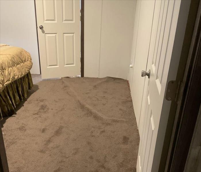Water-damaged carpet that is partially pulled up in a bedroom